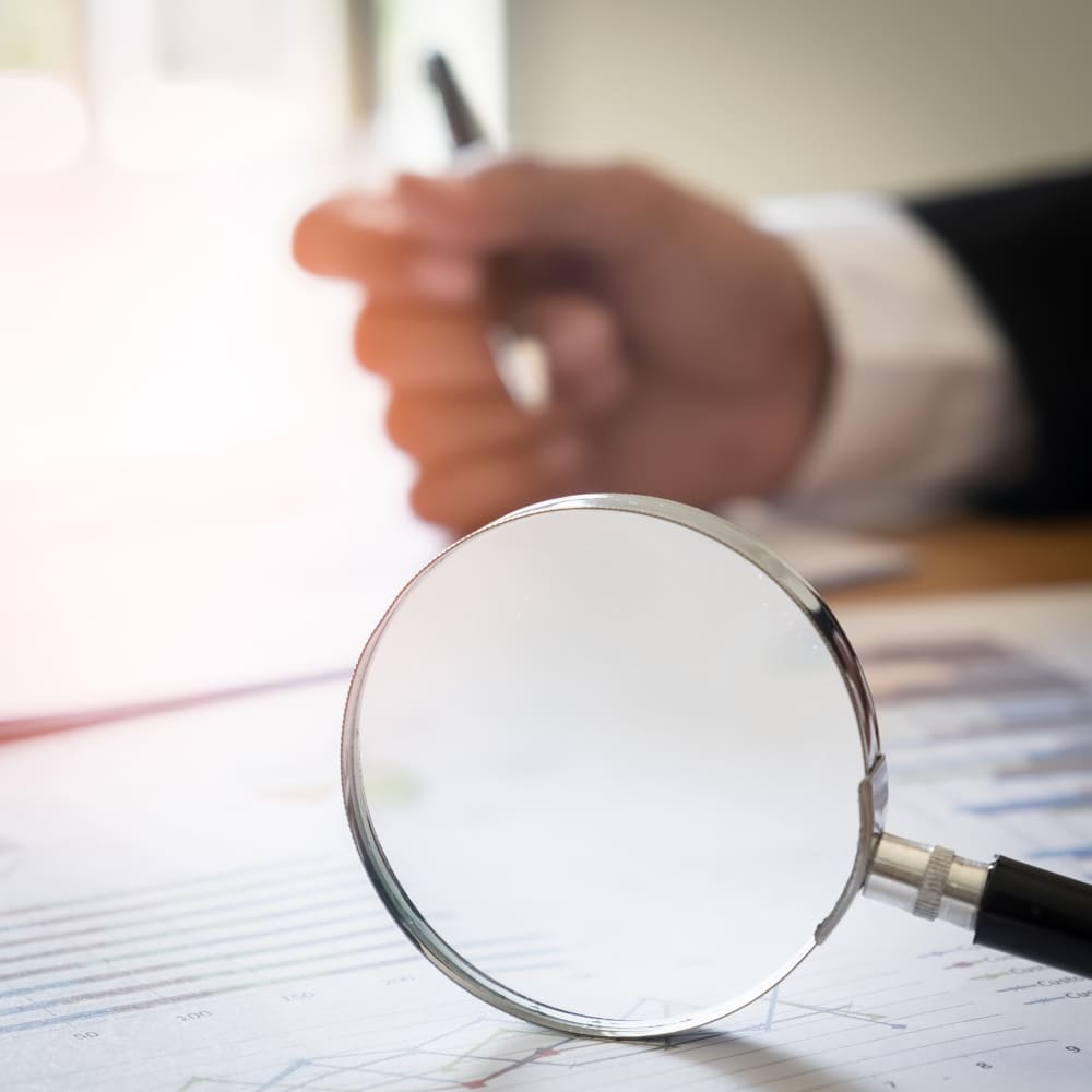 يد رجل يمسك قلم وبجانبه عدسة مكبرة يد رجل يمسك قلم وبجانبه عدسة مكبرة