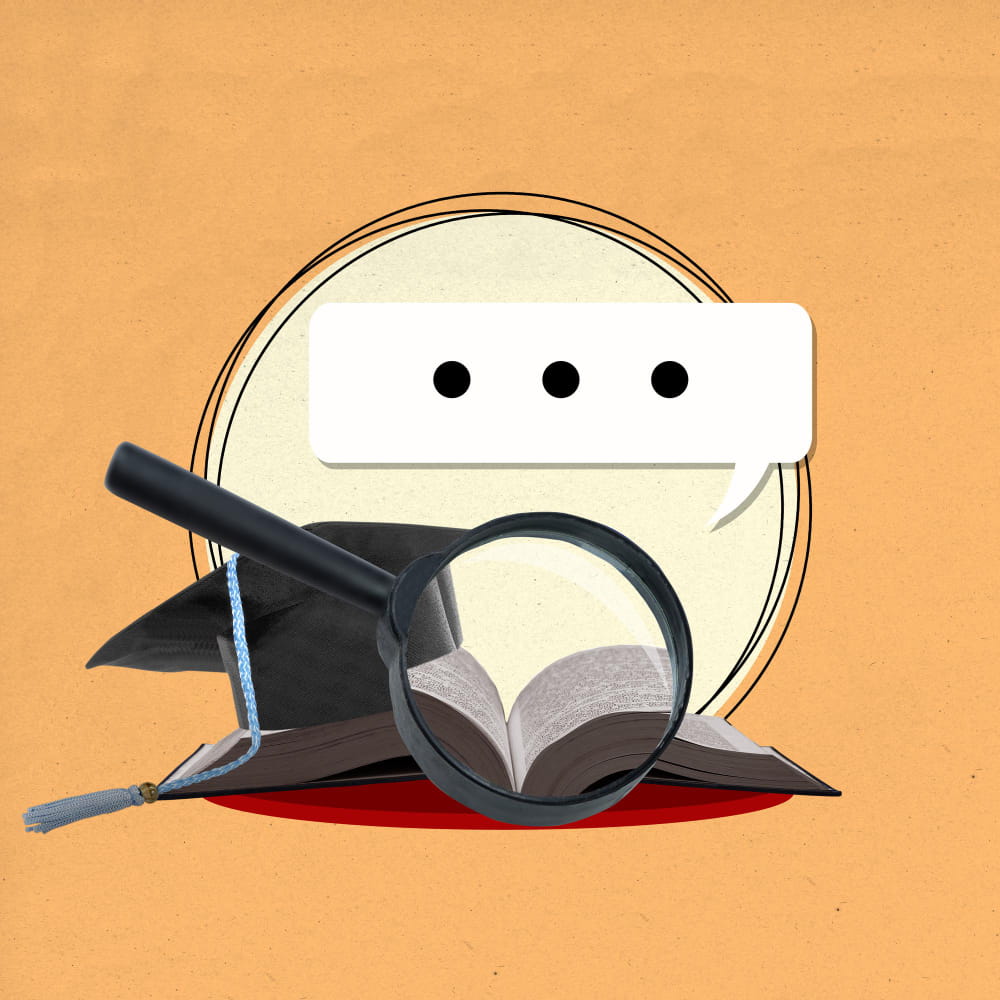 عدسة موجهة نحو كتاب مفتوح وبجانبه كاب تخرج