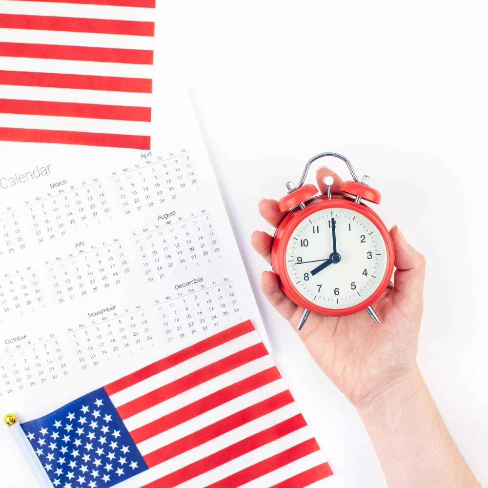 يد تمسك منبه وبجانبها تقويم وعلم أمريكا