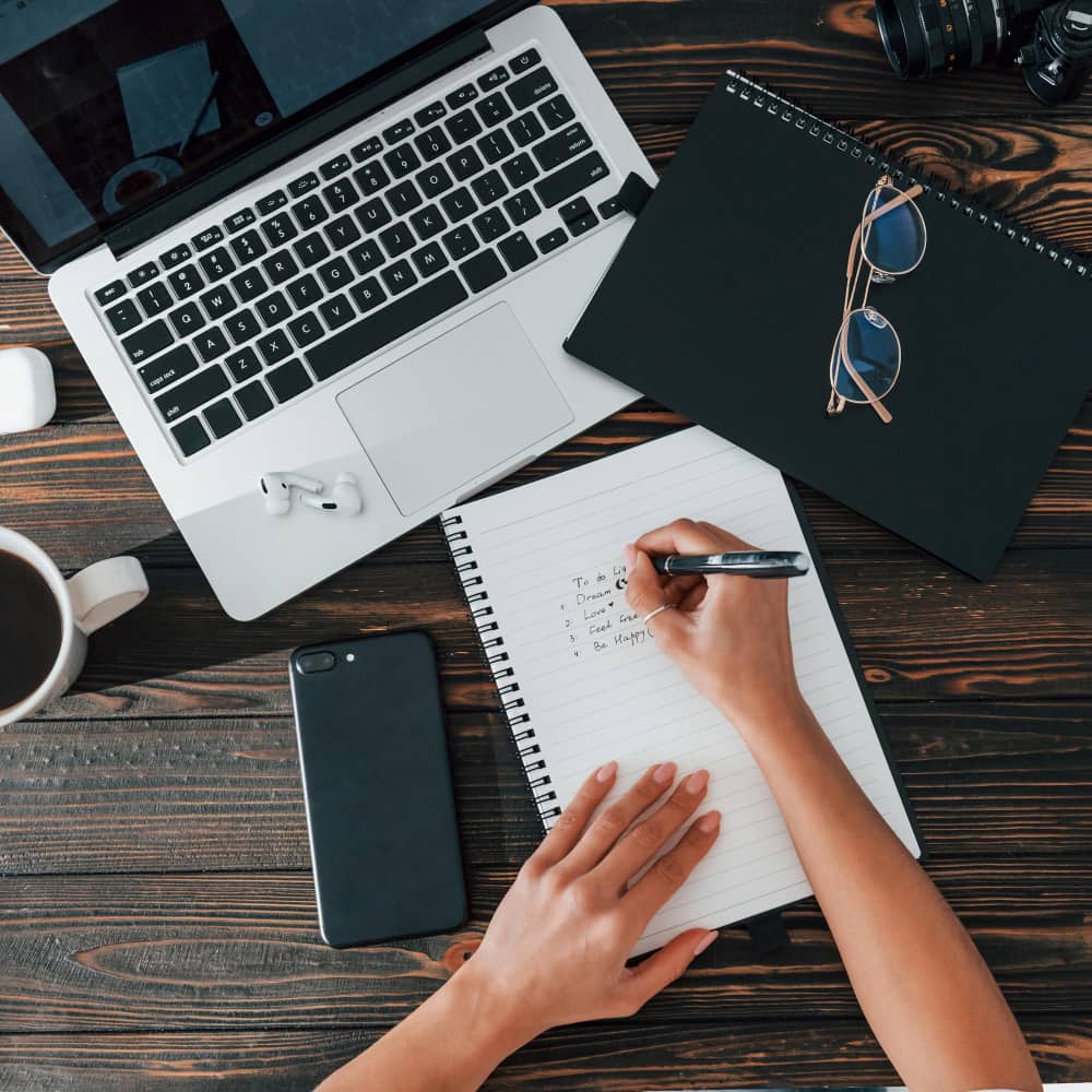 فتاة تكتب بالقلم على ورقة وأمامها لاب توب